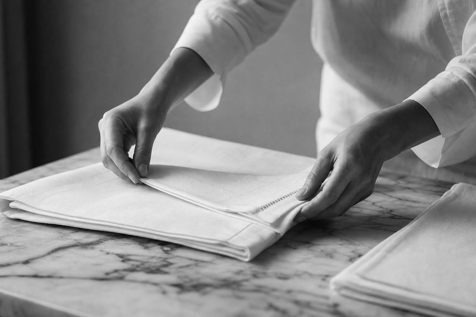 Hands folding crisp white linen on a marble surface